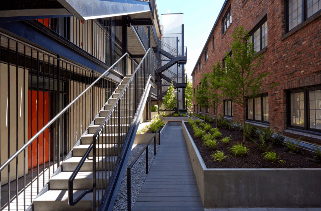Modern exterior walkway and stairwell at multifamily complex with updated landscaping and historic brick facade in Seattle