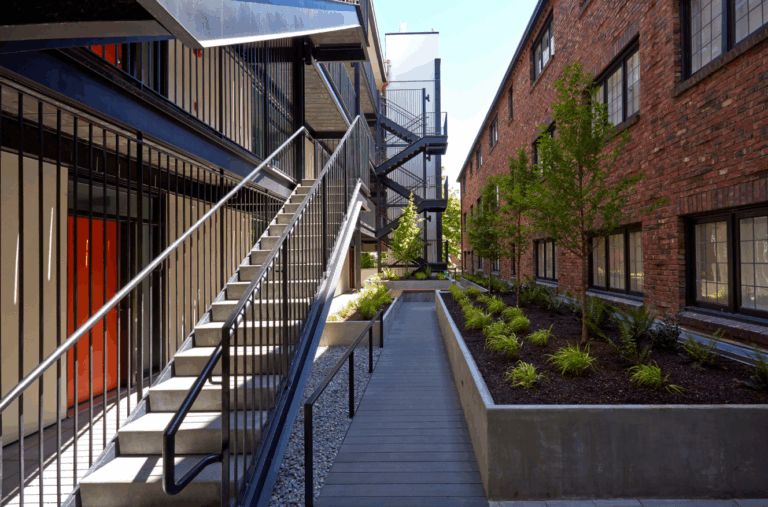 Modern exterior walkway and stairwell at multifamily complex with updated landscaping and historic brick facade in Seattle