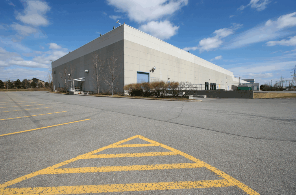 Exterior view of stabilized industrial warehouse facility with large parking lot and loading docks, part of a family office real estate portfolio